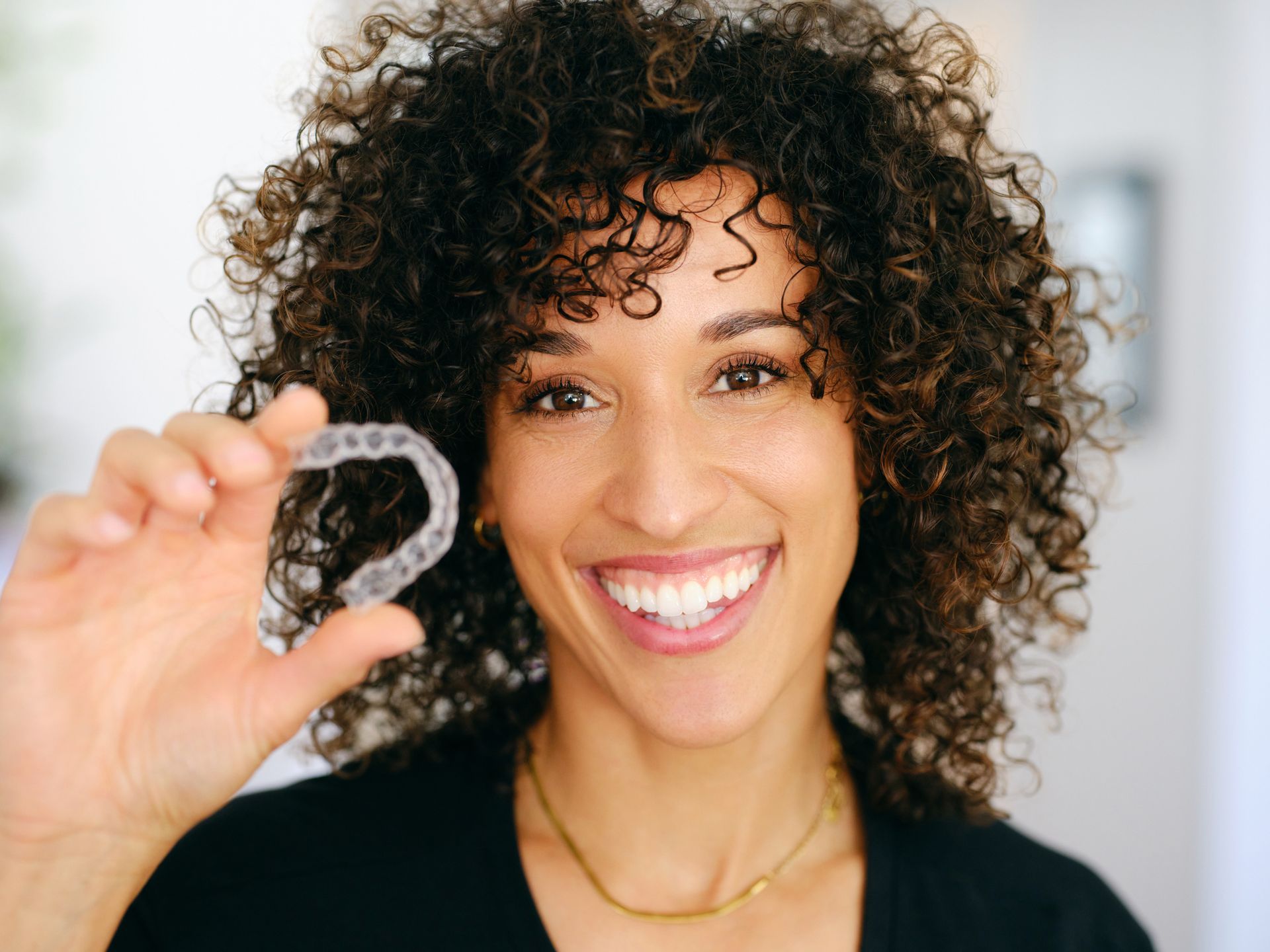 A woman with curly hair is holding a clear brace in her hand.
