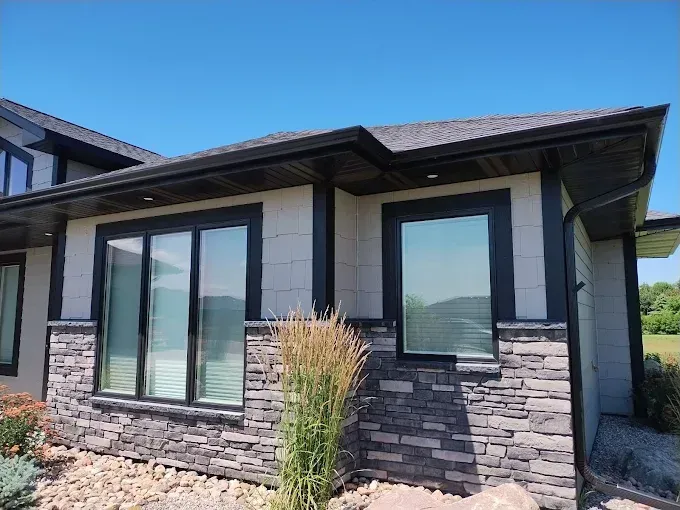 Modern house exterior with stone facade and black window frames under a blue sky.