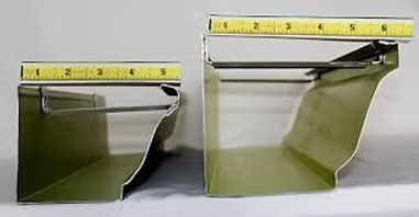 Two green metal gutters of different sizes with rulers on top.