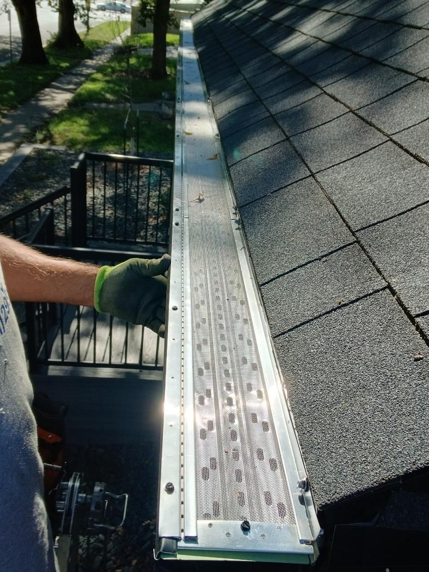 A person installing a metal gutter guard along a rooftop edge.