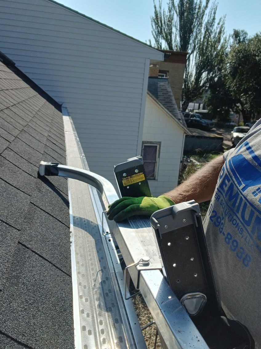 Person cleaning a gutter, using a ladder on a sunny day.