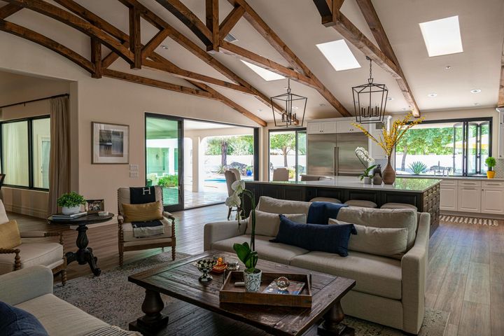 Bright open living room with vaulted wood beams, sofas, coffee table, and large windows overlooking greenery