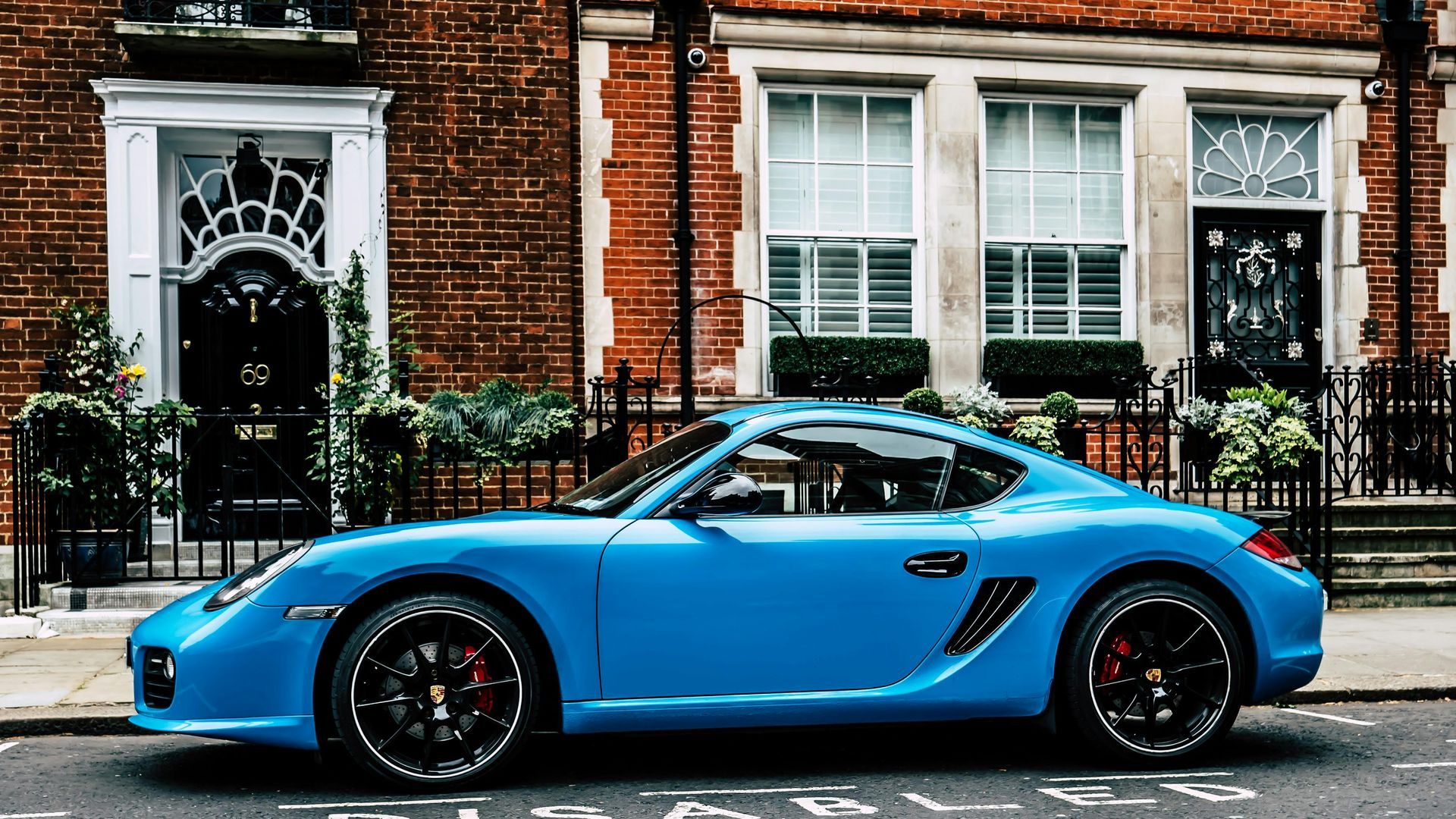 Blue Porsche sports car parked on a London street in front of a brick building.