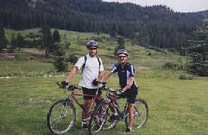 A man and a woman are standing next to their bicycles in a grassy field.