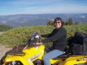 A woman is riding a yellow atv on a dirt road.