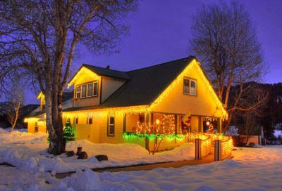 A yellow house is decorated with christmas lights in the snow.