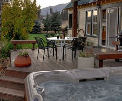 A hot tub is on a deck next to a table and chairs.