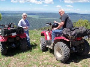 A man and a woman are riding atvs on top of a hill.