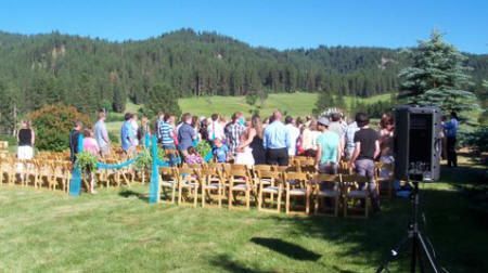 A large group of people are standing in a field watching a wedding ceremony.