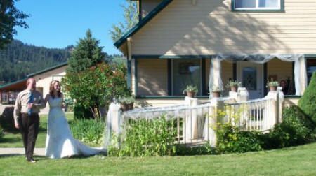 A bride and groom are walking in front of a house.