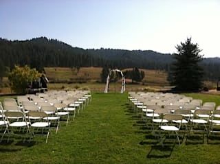 A row of folding chairs are lined up in a grassy field with mountains in the background.