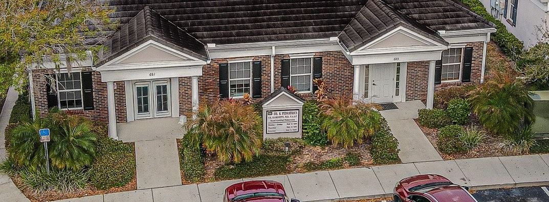 Modern glass building reflecting the sky, with lush green bushes in front.