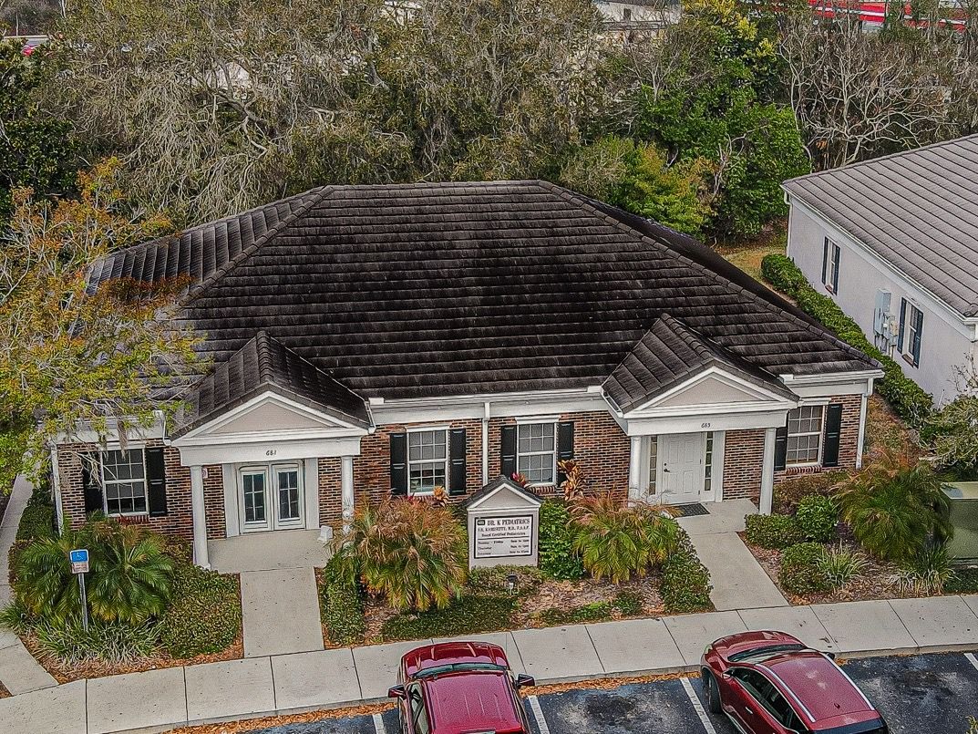 Aerial view of a small brick office building with white columns, a dark roof, and parked cars out front