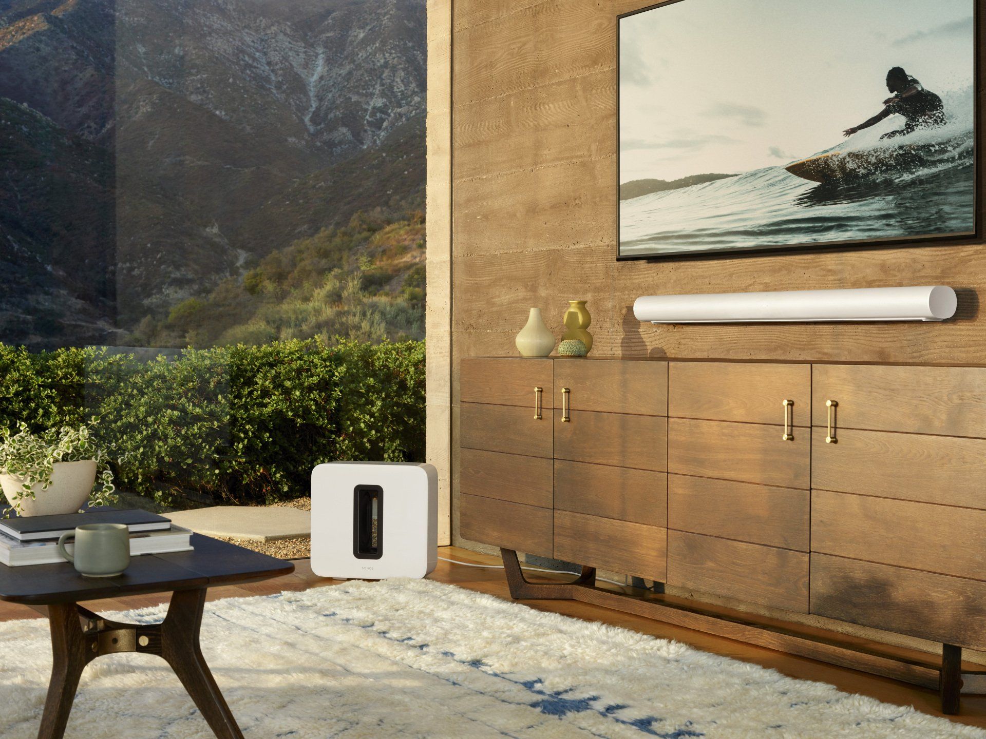 Living room with speaker, TV, and mountain view. White rug, wood cabinets, and surf art.