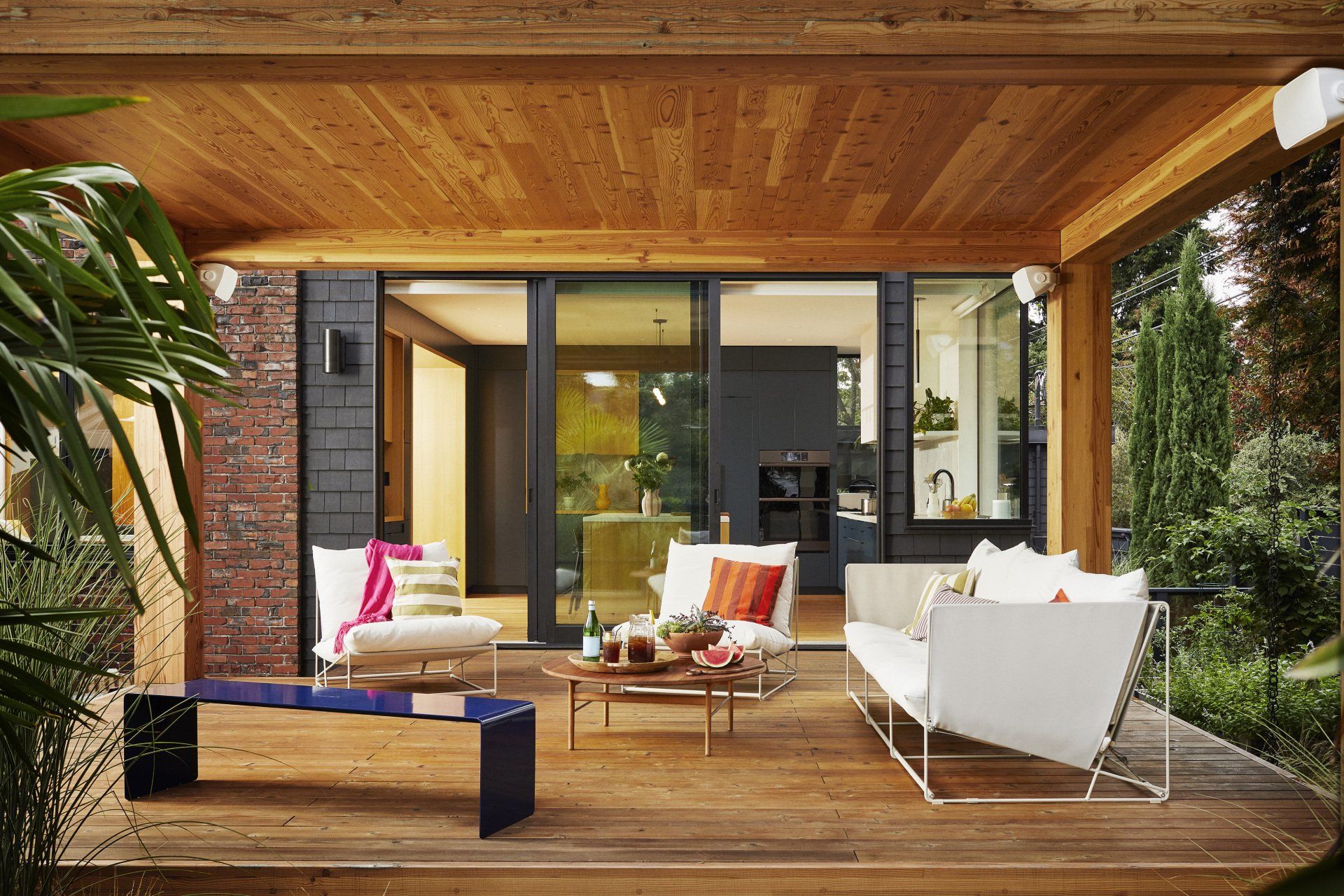 Wooden deck with white outdoor furniture, view into a modern home with kitchen.