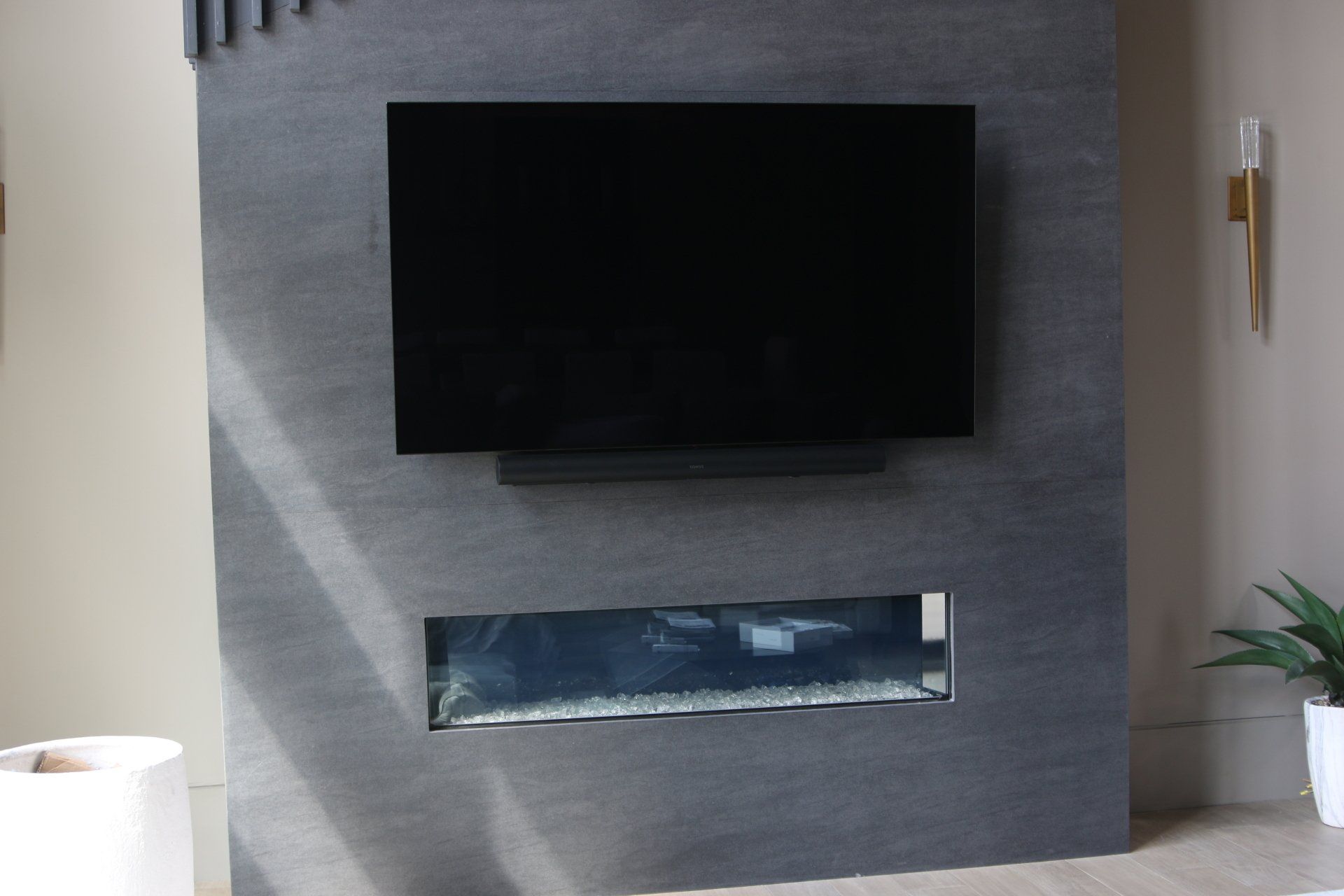 Large flat-screen TV and soundbar mounted above a modern fireplace, set in a gray stone wall.