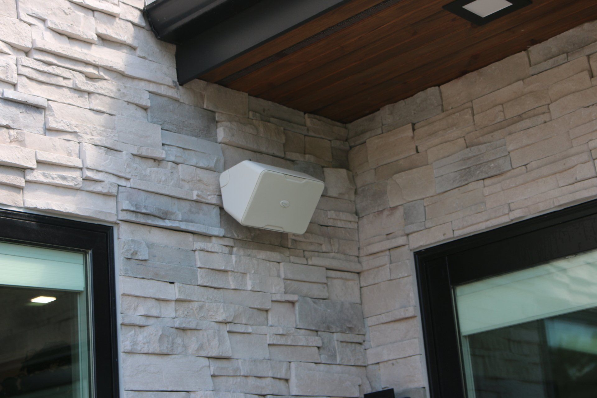 White outdoor speaker mounted on light stone exterior wall.