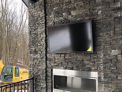TV mounted on a dark stone wall above a fireplace; construction equipment visible in the background.