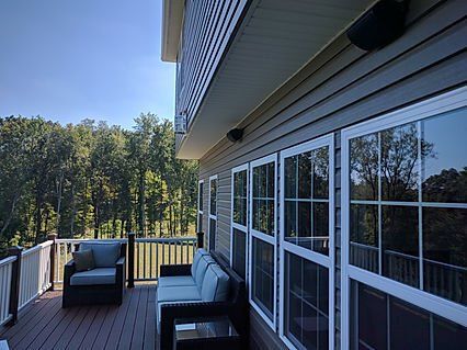 Deck with outdoor furniture, windows, speakers, and a view of trees under a blue sky.