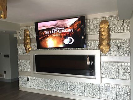 TV mounted above a fireplace on a decorative textured wall, with gold sconces on either side.