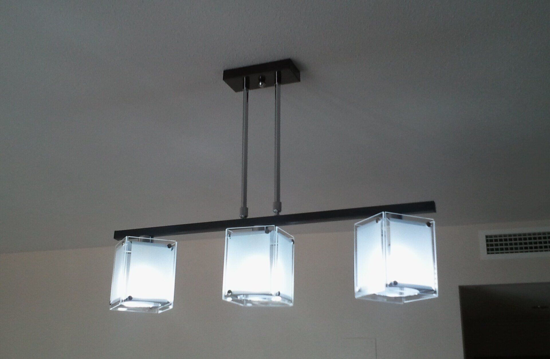 Lámpara colgante de tres luces con pantallas cuadradas esmeriladas, estructura negra y soporte de techo.