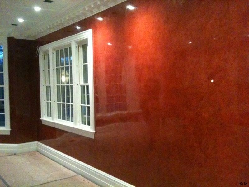 Pared roja brillante con molduras blancas y ventana, iluminada por focos en el techo.