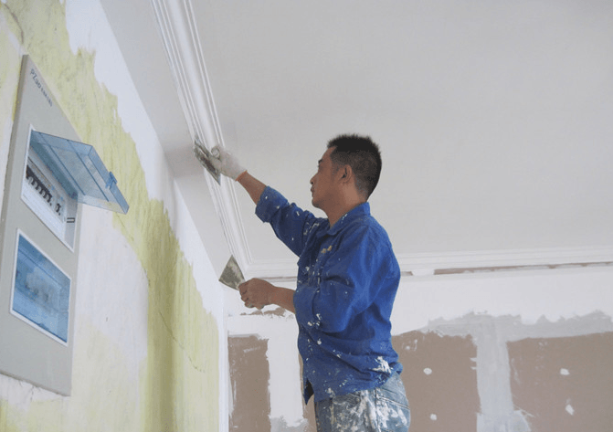 Hombre con mono azul utilizando una llana para aplicar yeso a una moldura en una pared.