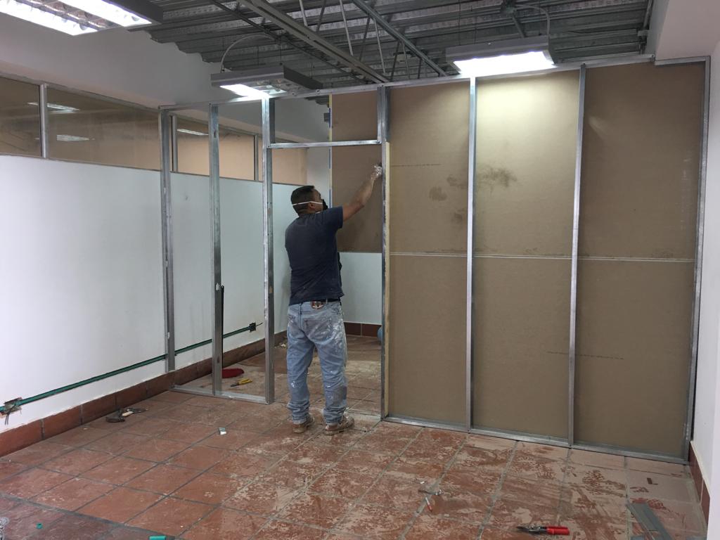 Hombre instalando paneles de yeso en una habitación con estructura metálica. Obra en curso, con herramientas a la vista.