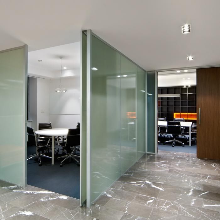 Oficina con paredes de cristal esmerilado, sala de reuniones y espacio de trabajo a la vista. Suelo de mármol.