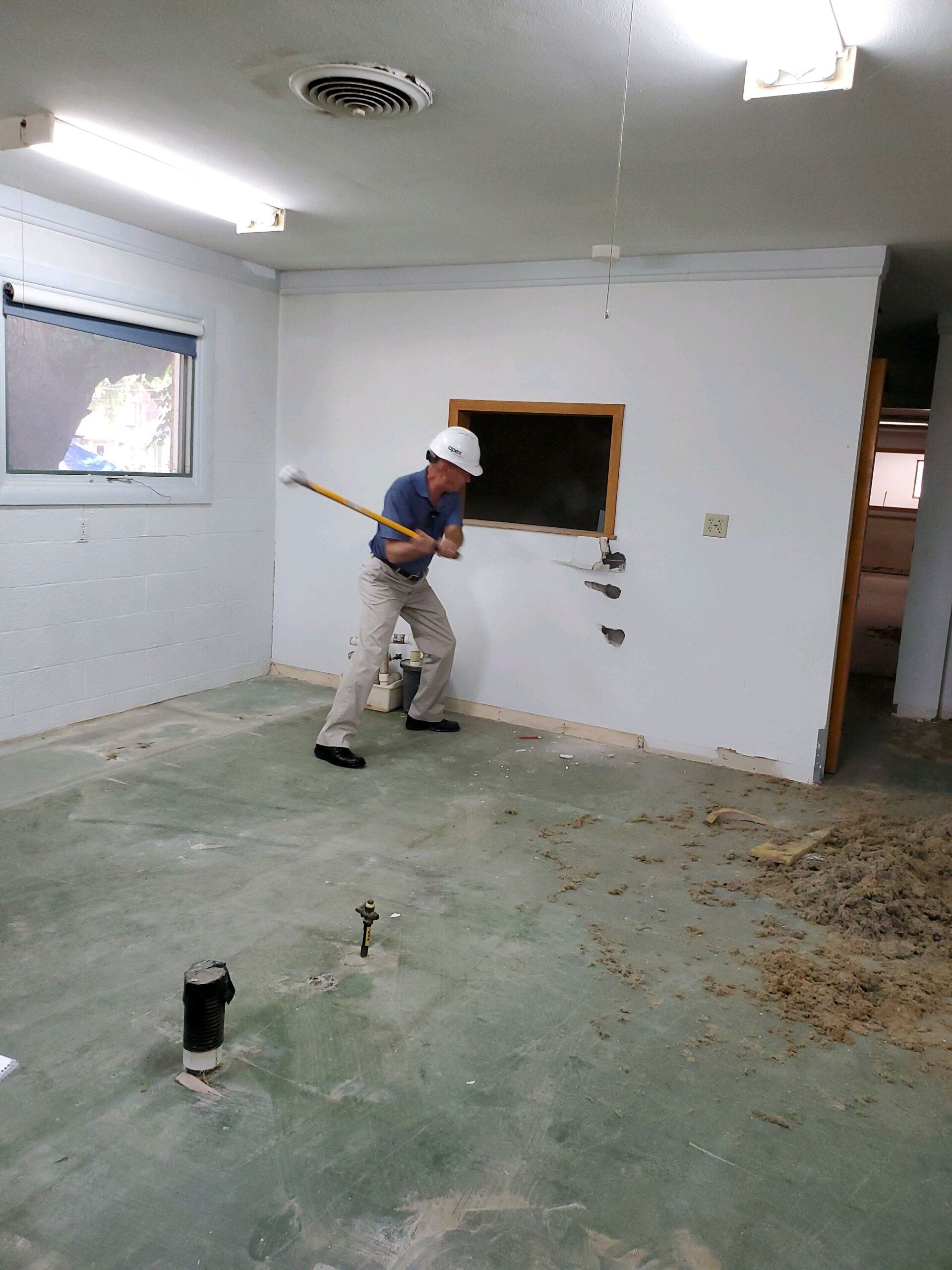 Persona con casco derribando una pared con una maza dentro de una habitación.