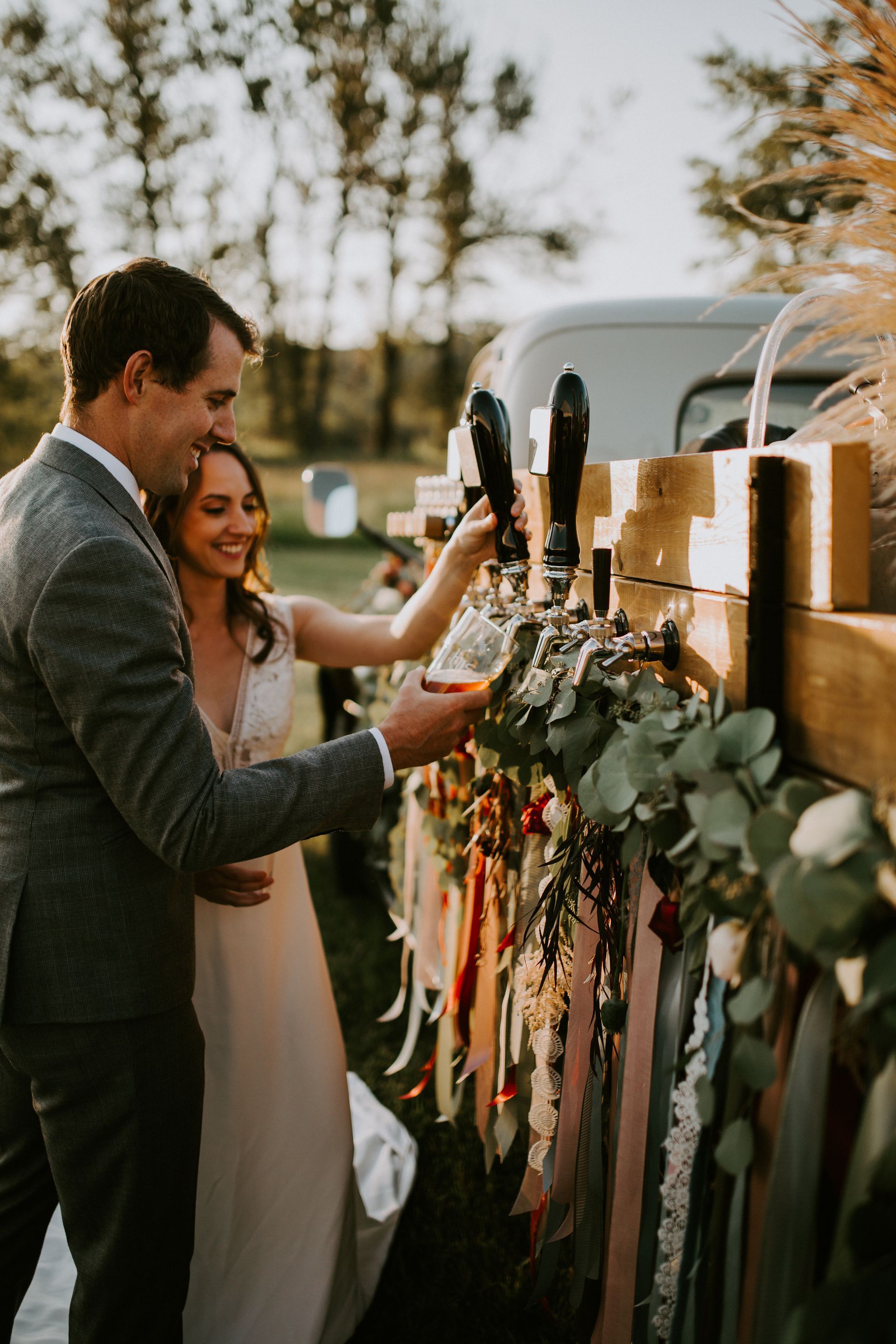 A bride and groom are pouring beer from a tap at their wedding.