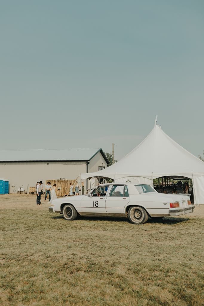 A white car is parked in a grassy field in front of a white tent.