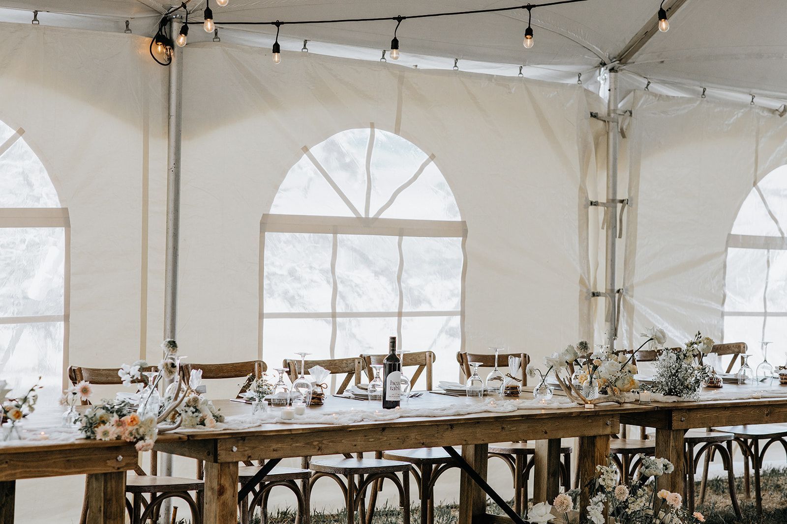 A long wooden table is sitting under a white tent.