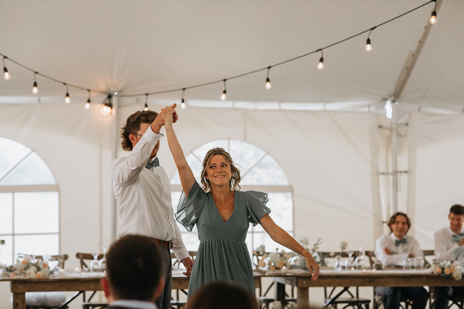 A man and a woman are dancing in a tent at a wedding reception.