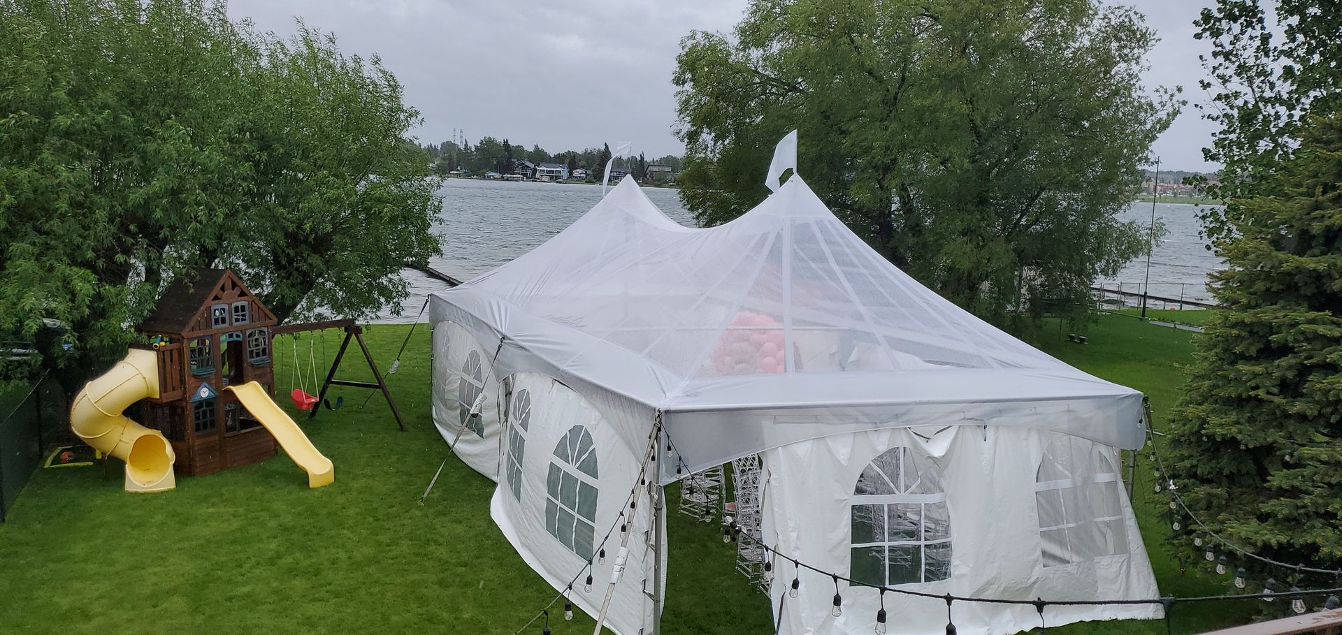 A white tent is sitting on top of a lush green field next to a playground.