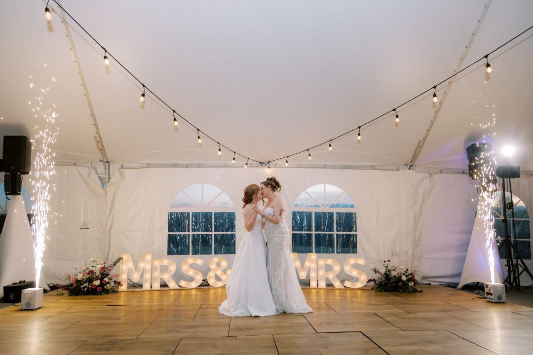 A bride and groom are kissing under a tent at their wedding reception.