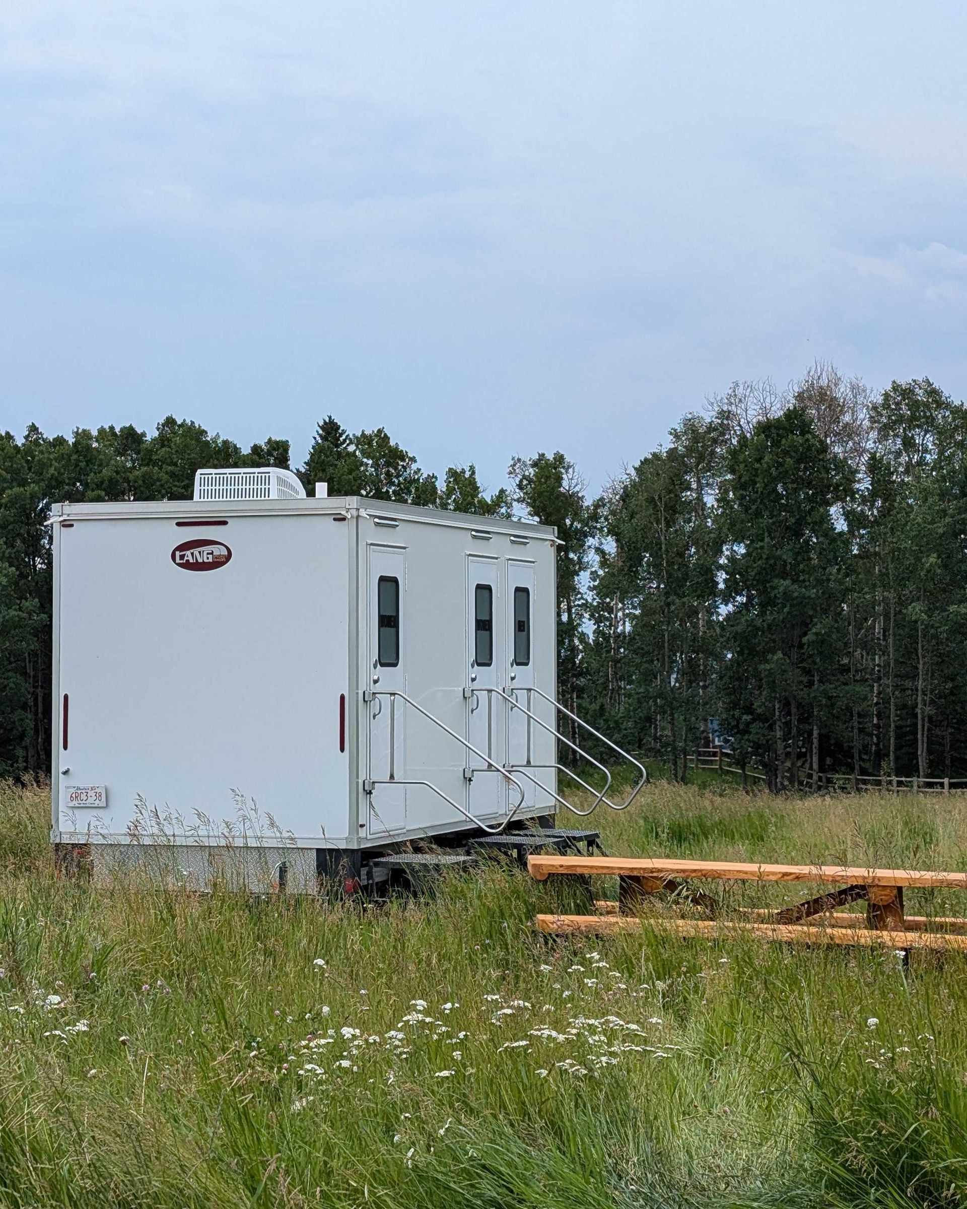A white trailer is parked in a grassy field next to a picnic table.
