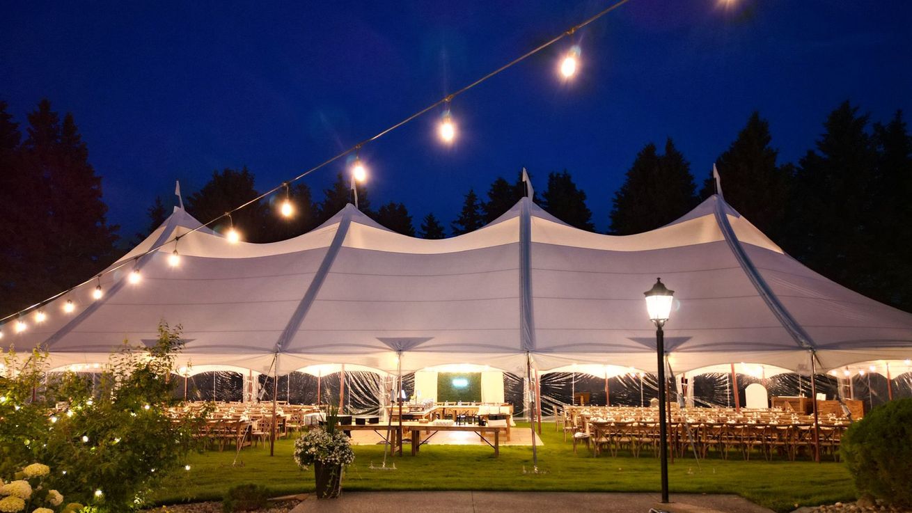 A large white tent is lit up at night with lights hanging from the ceiling.