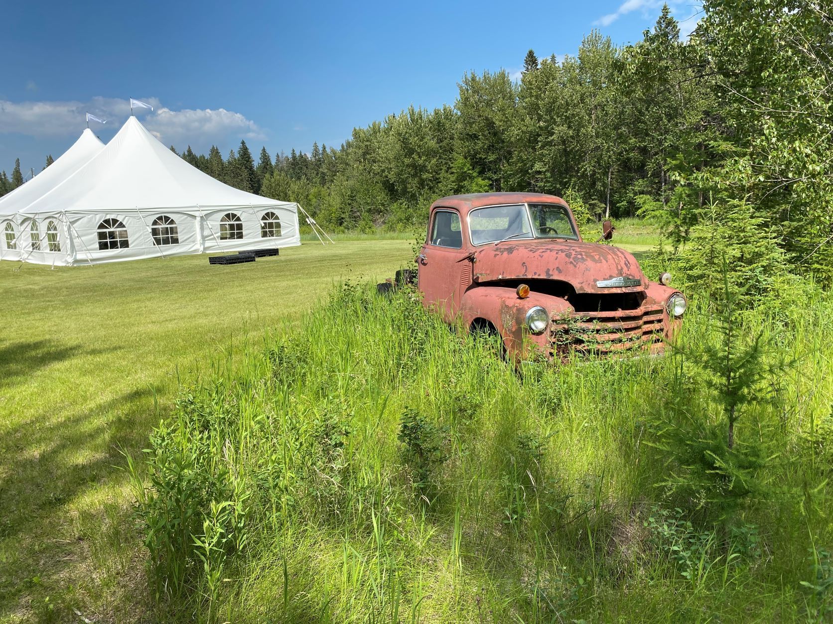 A red truck is parked in a grassy field next to a white tent.