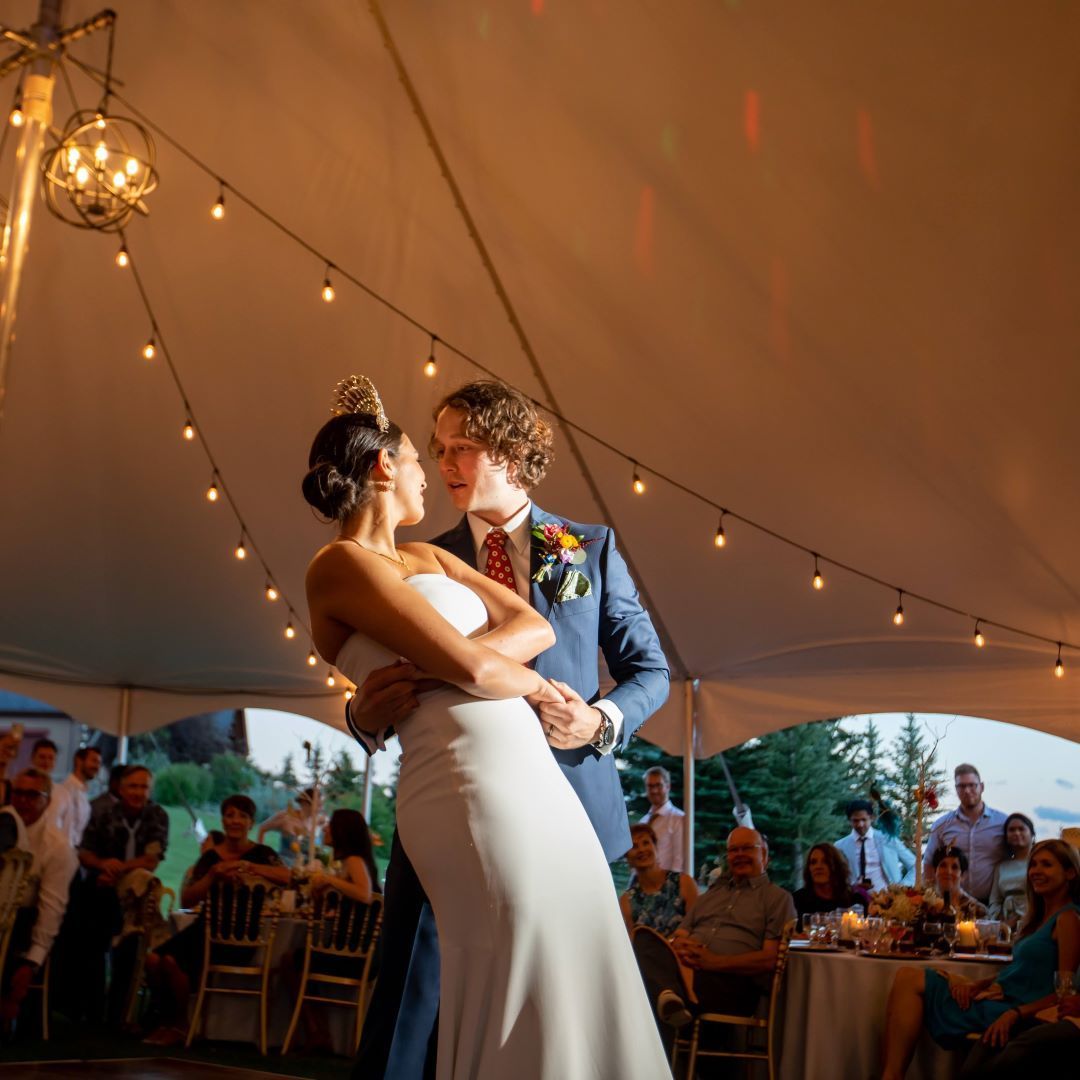 A bride and groom are dancing under a tent at their wedding reception.