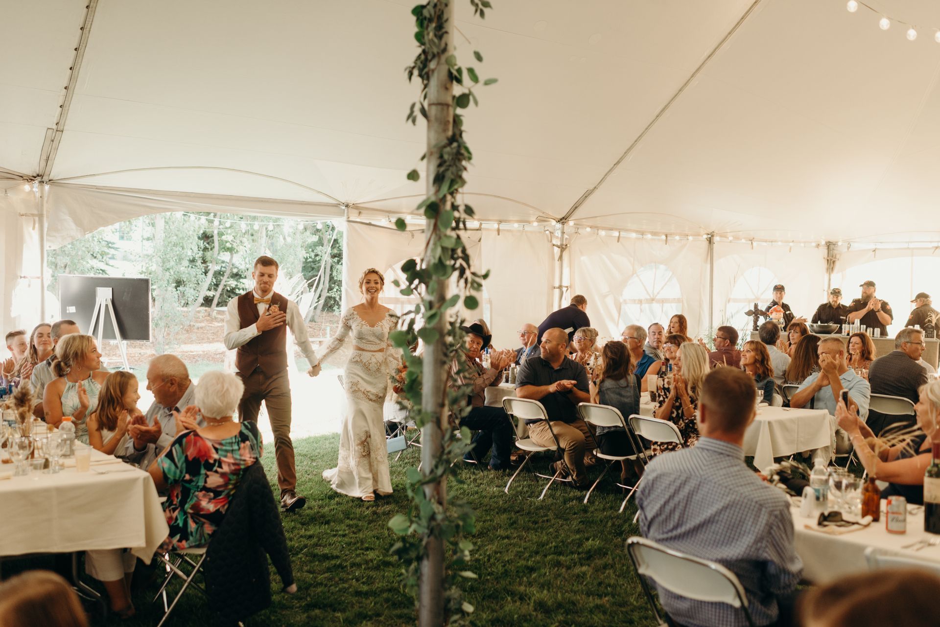 A bride and groom are walking down the aisle at a wedding reception under a tent.