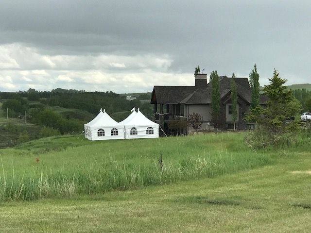 There are two tents in the middle of a grassy field in front of a house.