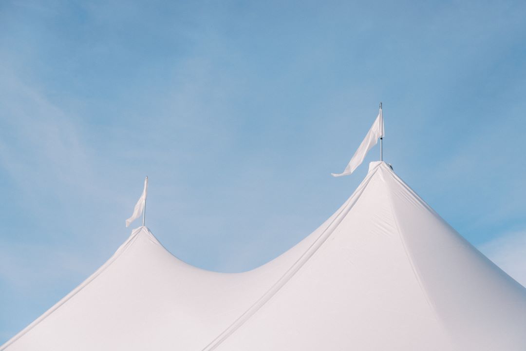 A white tent with two flags on top of it against a blue sky.