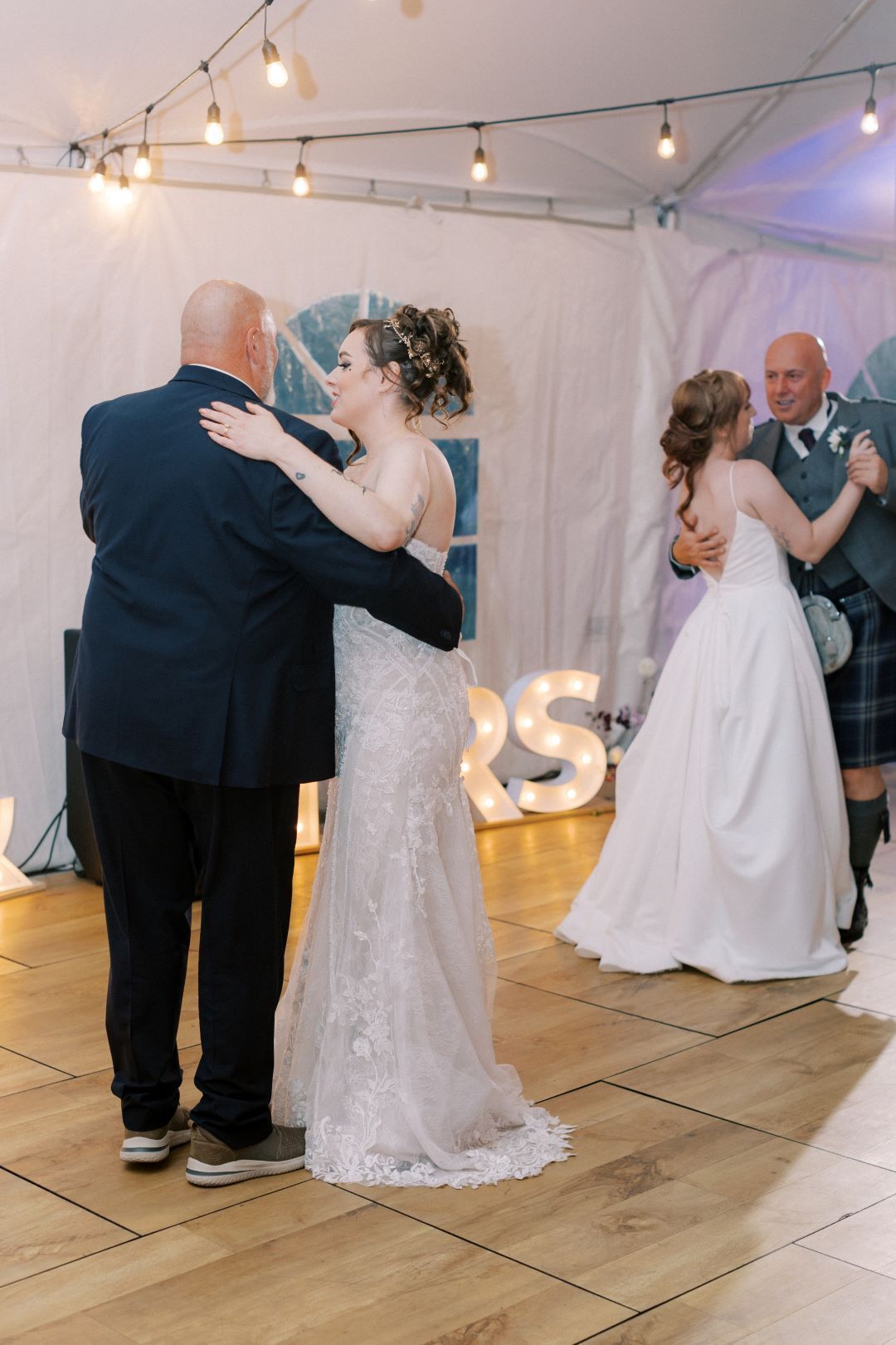 A bride and groom are dancing on a wooden floor at their wedding reception.