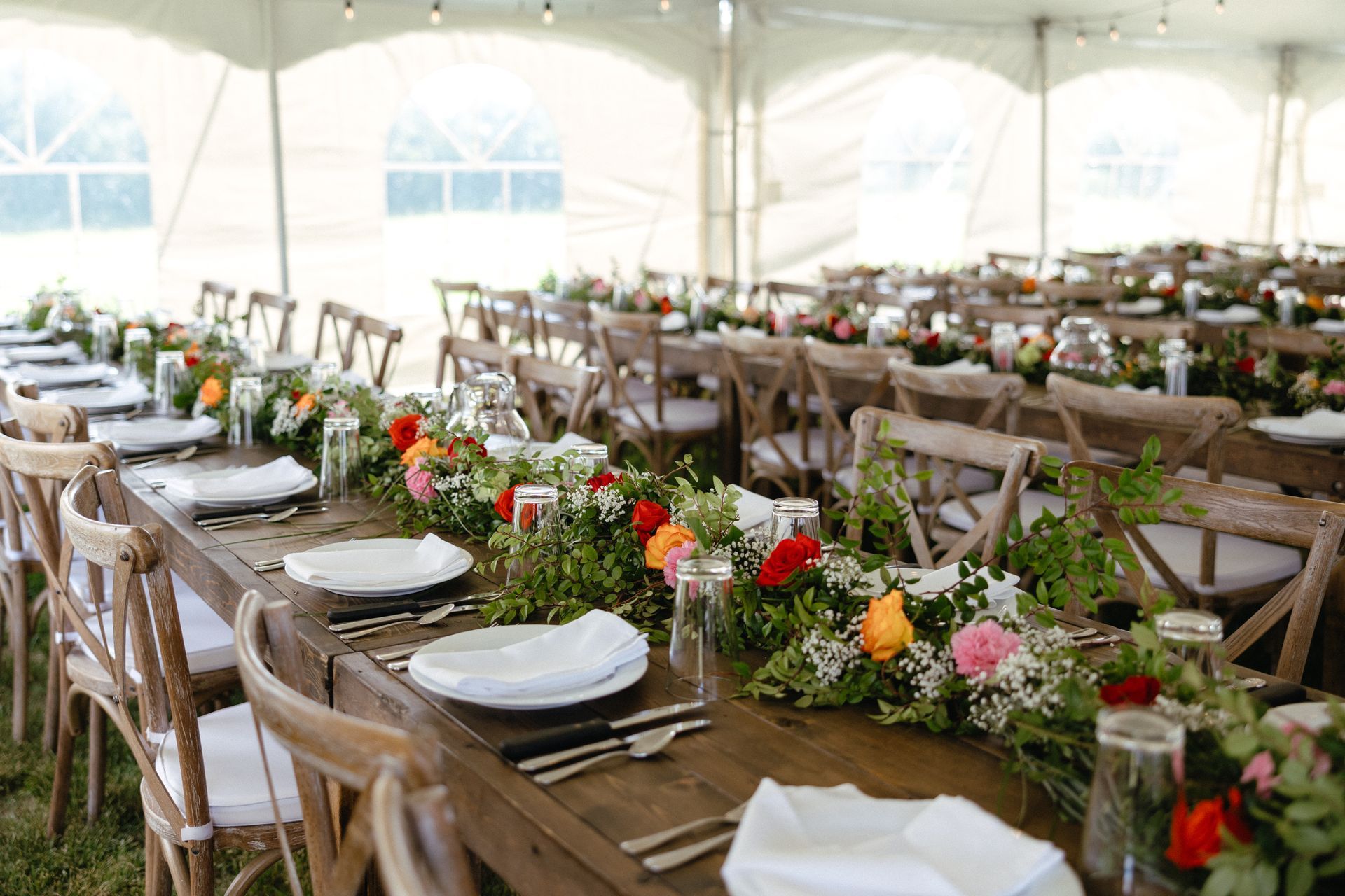 A long wooden table is set for a wedding reception under a tent.