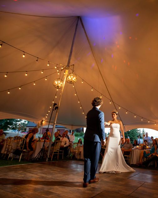 A bride and groom are dancing under a tent at their wedding reception.