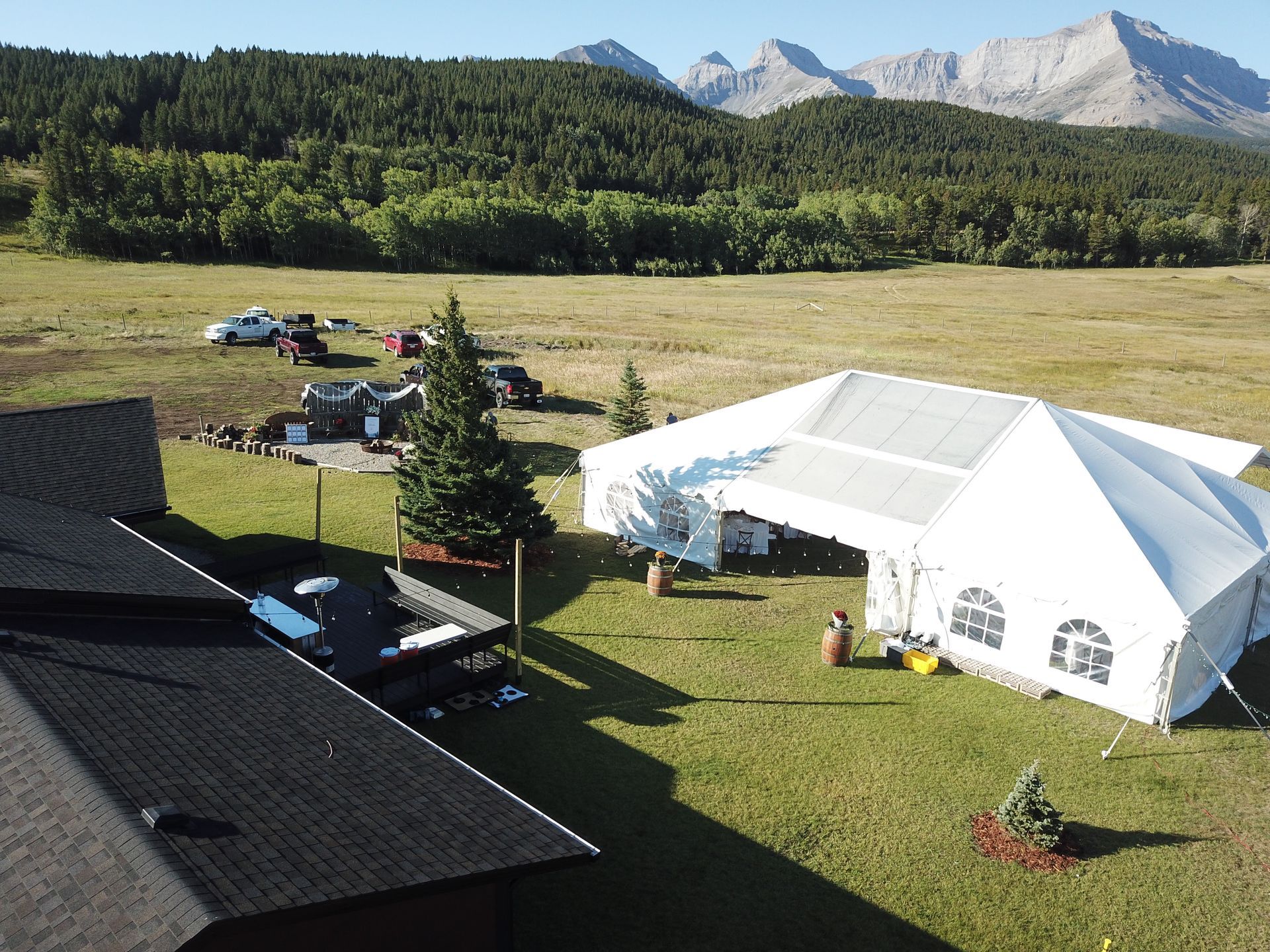 An aerial view of a large white tent in a grassy field with mountains in the background.