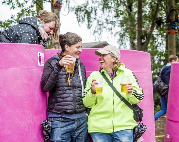 Two women are leaning against a pink wall drinking beer.