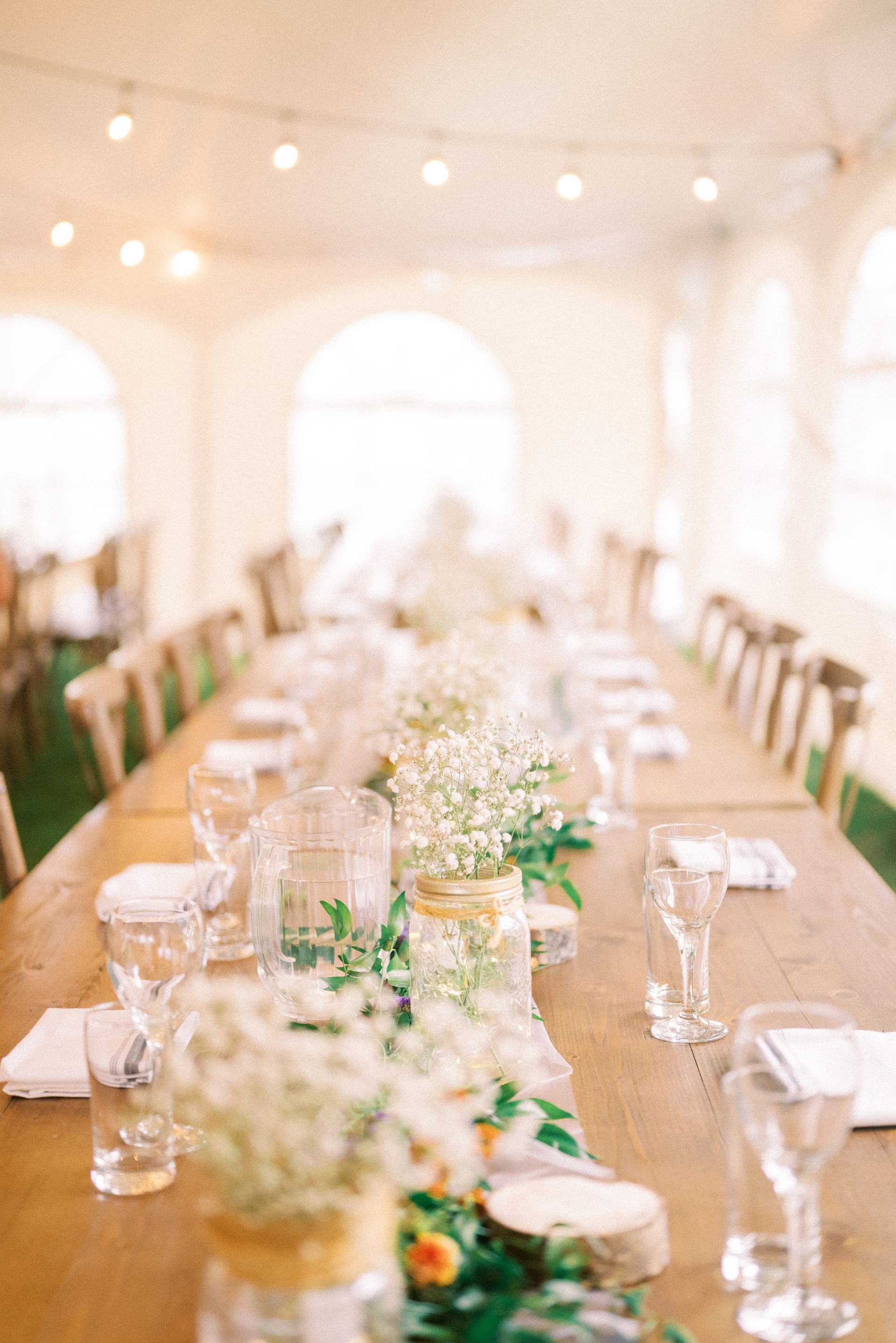 A long wooden table with flowers and glasses on it in a tent.