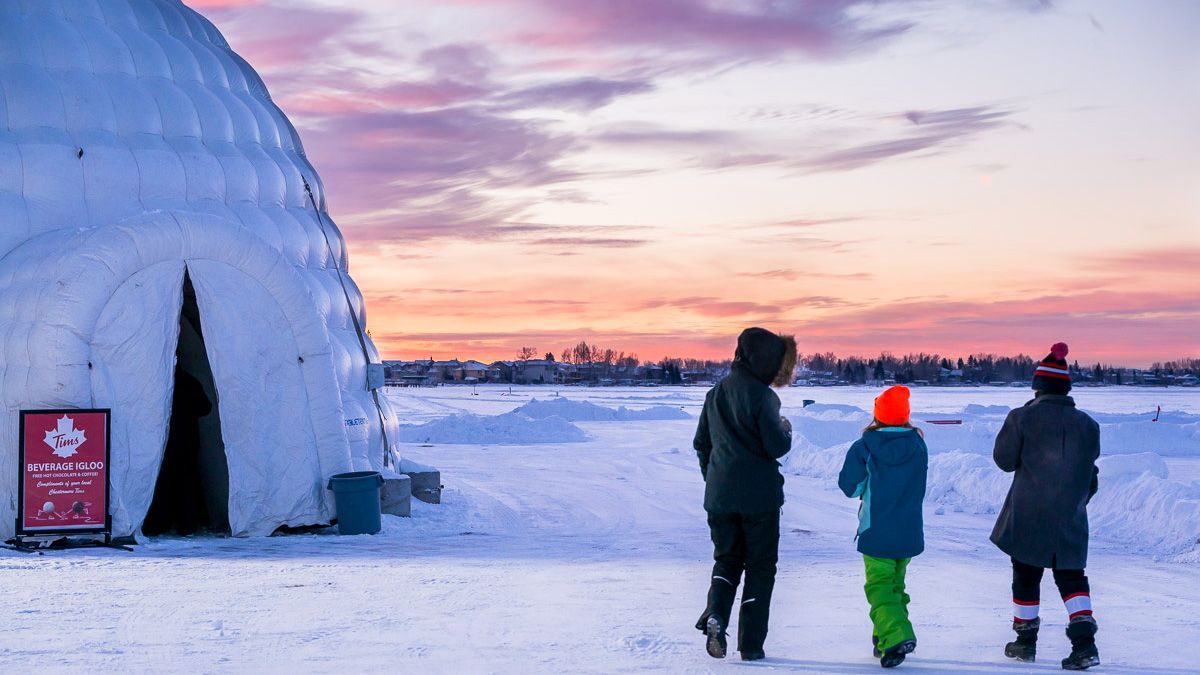 A group of people are standing in the snow in front of an igloo.